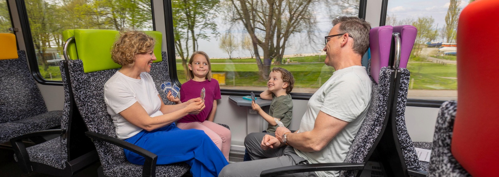 Familie reist zufrieden mit den Kindern im Thurbo Zug, sie spielen ein Kartenspiel.