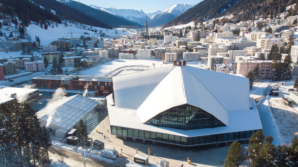 Verschneites, grosses Gebäude in einem Bergdorf mit Talsicht und Berge im Hintergrund.